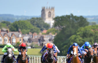 Horses in running at Beverley racecourse with the church in the distance