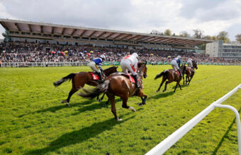 Runners in The bet365 Select Hurdle passing the packed grandstands at Sandown