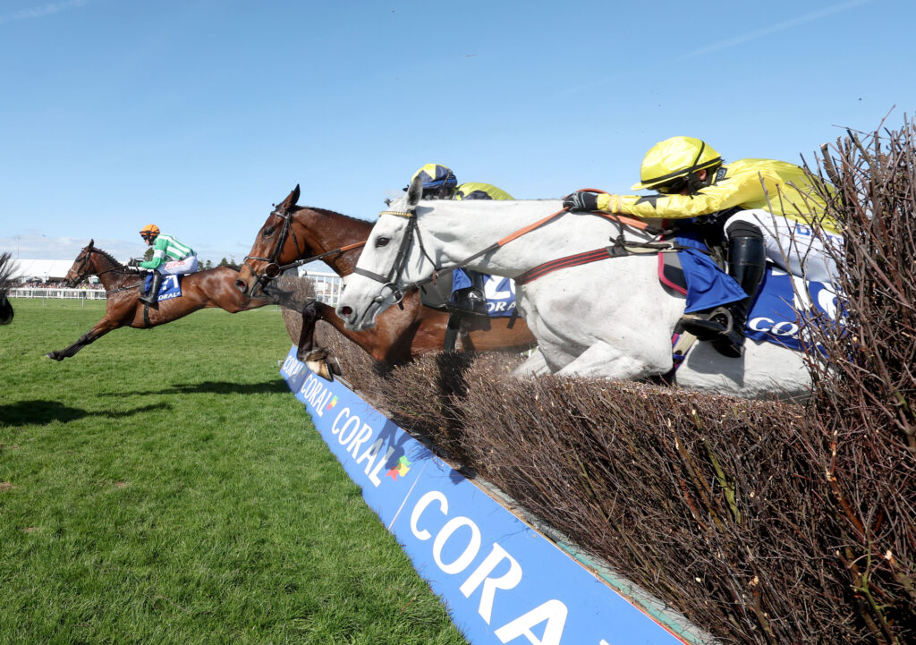 Macdermott and Danny Mullins (orange cap) winning The Coral Scottish Grand National Handicap Chase at Ayr, with two horses just behind, mid jump over a fence.